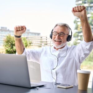Excited older business man looking at laptop raising fists winning online.